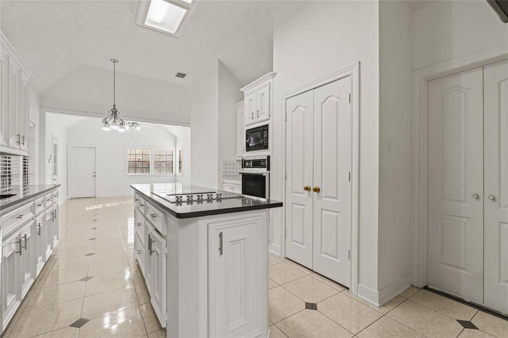 This beautifully designed kitchen flows effortlessly into the breakfast and living areas, making it the heart of the home. The sleek black countertops contrast elegantly with the crisp white cabinetry, offering a modern yet timeless appeal. A spacious island with a built-in cooktop provides additional prep space, while the skylights above bathe the room in natural light. The pantry and extra storage closets ensure organization is a breeze.