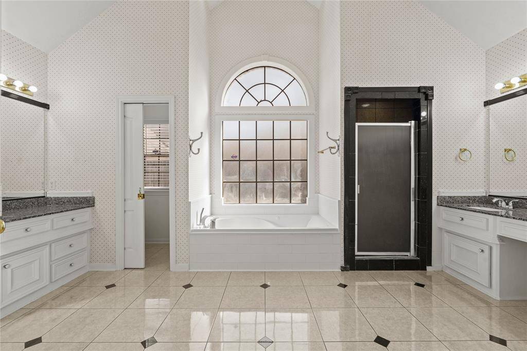 This luxurious primary bathroom is a private retreat designed for relaxation and convenience.The elegant arched window bathes the space in natural light, perfectly complementing the spa-like soaking tub below. Dual vanities with granite countertops offer ample space for morning routines, while the separate glass-enclosed shower adds both style and functionality. The high vaulted ceiling enhances the spacious feel, making this bathroom a true sanctuary.