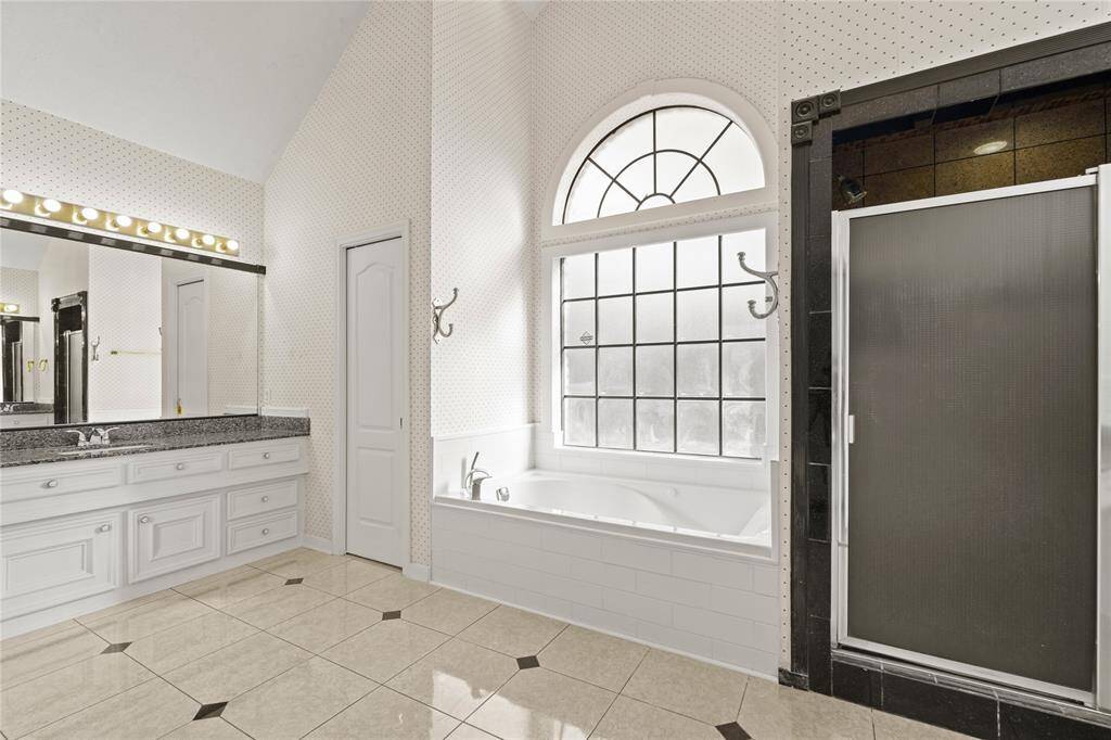 This spa-like primary bathroom is designed for both luxury and relaxation. The elegant arched window floods the space with natural light, creating a serene ambiance for the deep soaking tub below. A spacious walk-in shower with sleek black tile accents adds a modern touch, while the dual vanity with granite countertops provides ample space for daily routines. The high ceilings enhance the airy, open feel, making this a perfect retreat for unwinding at the end of the day.