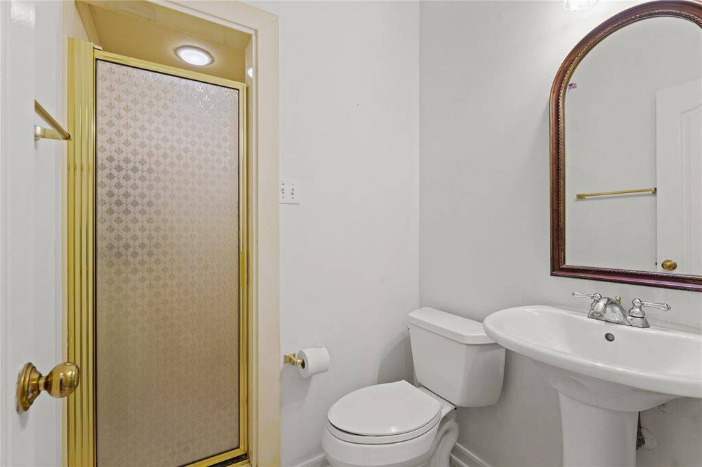 This charming guest bathroom offers both convenience and elegance in a compact design. The classic pedestal sink adds a touch of sophistication, while the arched mirror with a rich wood frame enhances the warmth of the space. A sleek, enclosed shower with gold accents provides a private and functional bathing area, making this the perfect retreat for guests or family members.Thoughtfully designed with timeless finishes, this bath room is both stylish and practical.