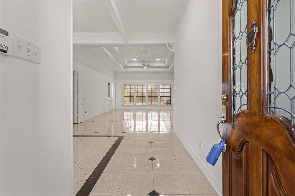Step into elegance as you enter this stunning home, where high ceilings, intricate tray details, and gleaming tile floors set the stage for a sophisticated yet inviting ambiance. The grand entryway opens seamlessly into the spacious living area, flooded with natural light from the large windows ahead. A beautiful glass-paneled wooden door adds a touch of classic charm, welcoming guests with warmth and style. The open-concept design ensures a smooth flow throughout the home.