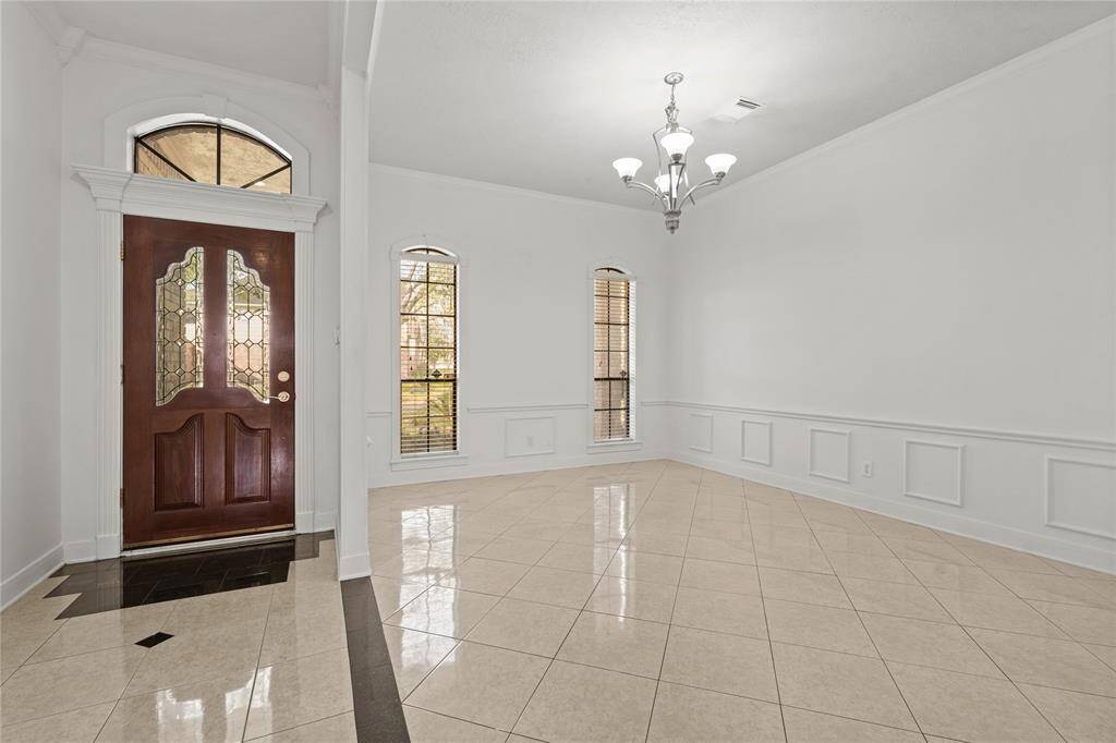 This elegant formal dining area is the perfect blend of sophistication and warmth. The stunning chandelier casts a soft glow over the space, while the wainscoting and crown molding add timeless architectural charm. Natural light flows in through the tall arched windows, creating a bright and inviting ambiance. The open layout seamlessly connects to the grand entrance, setting the stage for memorable dinners and special gatherings.