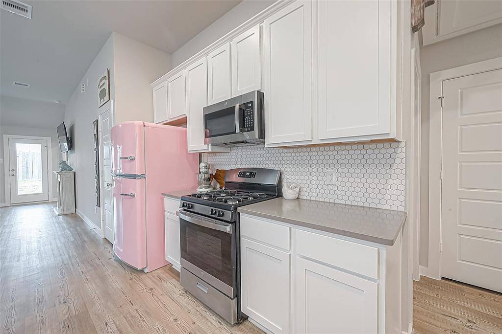 Closer view of kitchen. White cabinetry, quartz counters, hexagon tiled backsplash, gas range, built in microwave. Pink refrigerator will be replaced with a different refrigerator for tenant's convenience and use.