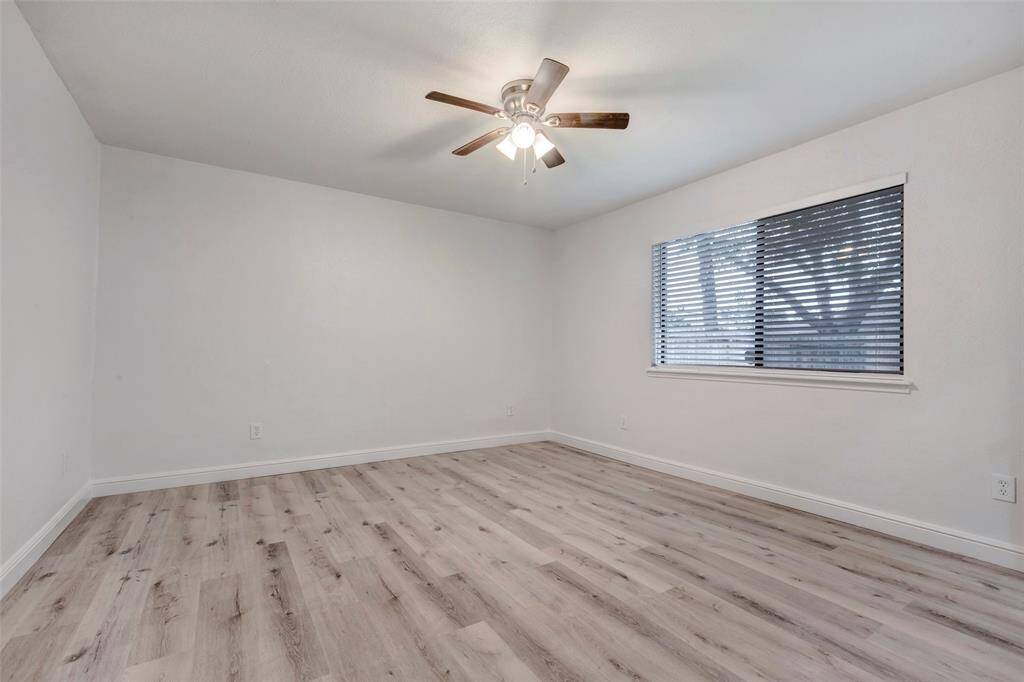 Primary bedroom features light laminate flooring, a ceiling fan with lights, and a window with blinds, offering a bright and airy space.