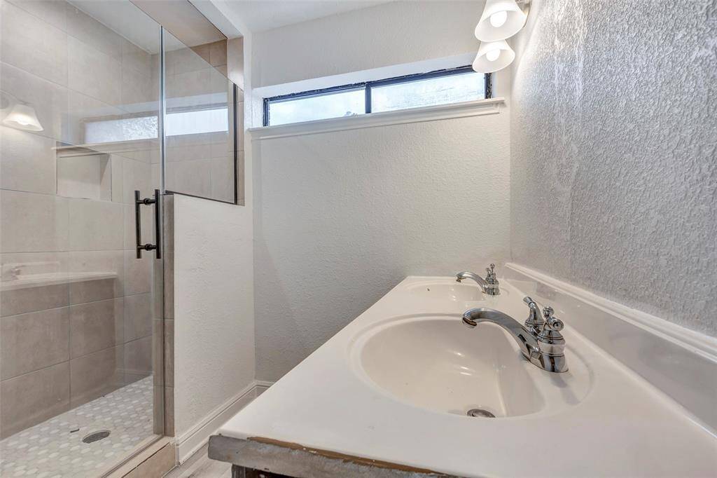 Primary bath features a modern glass-enclosed shower with tile walls and a built-in shelf. It also has a sleek dual-sink vanity and contemporary lighting, creating a bright and functional space. A lighted mirror to be added.