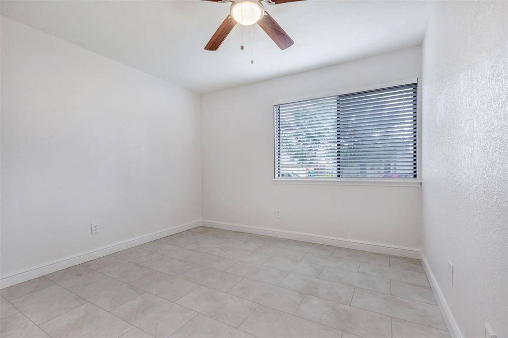 2nd bedroom features a clean, minimalist design with neutral tile flooring, white walls, a ceiling fan, and a window with blinds, offering a bright and versatile space.