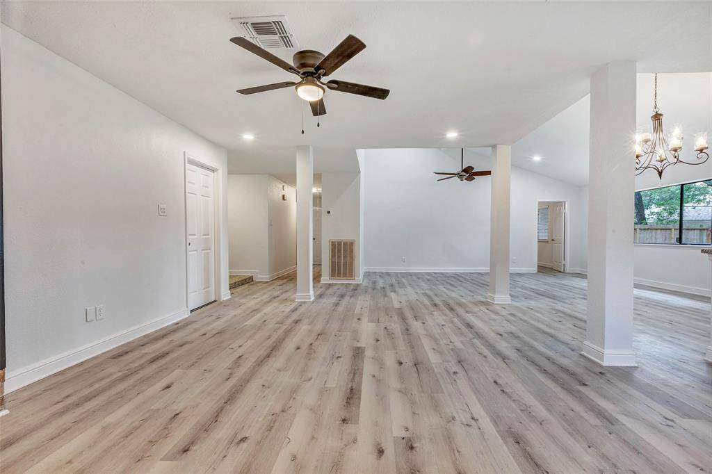 This living area features modern laminate flooring, neutral walls, and ceiling fans. It includes a dining space with a chandelier and large windows offering plenty of natural light.