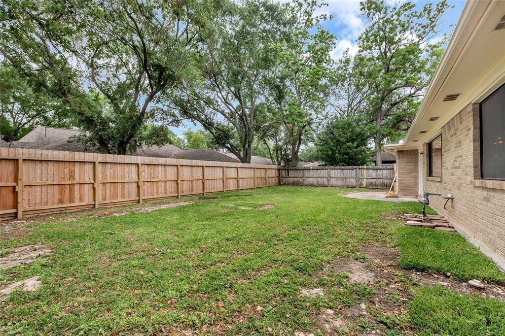 This photo shows a spacious backyard with a grassy lawn enclosed by a wooden fence. The house has a brick exterior and a patio area, ideal for outdoor activities.
