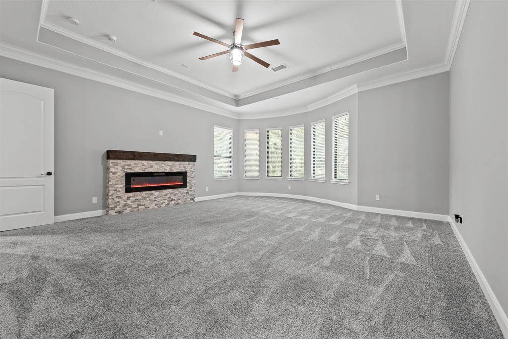 Primary bedroom with wood mantel and stone fireplace, decked ceiling and extended space at windows.
