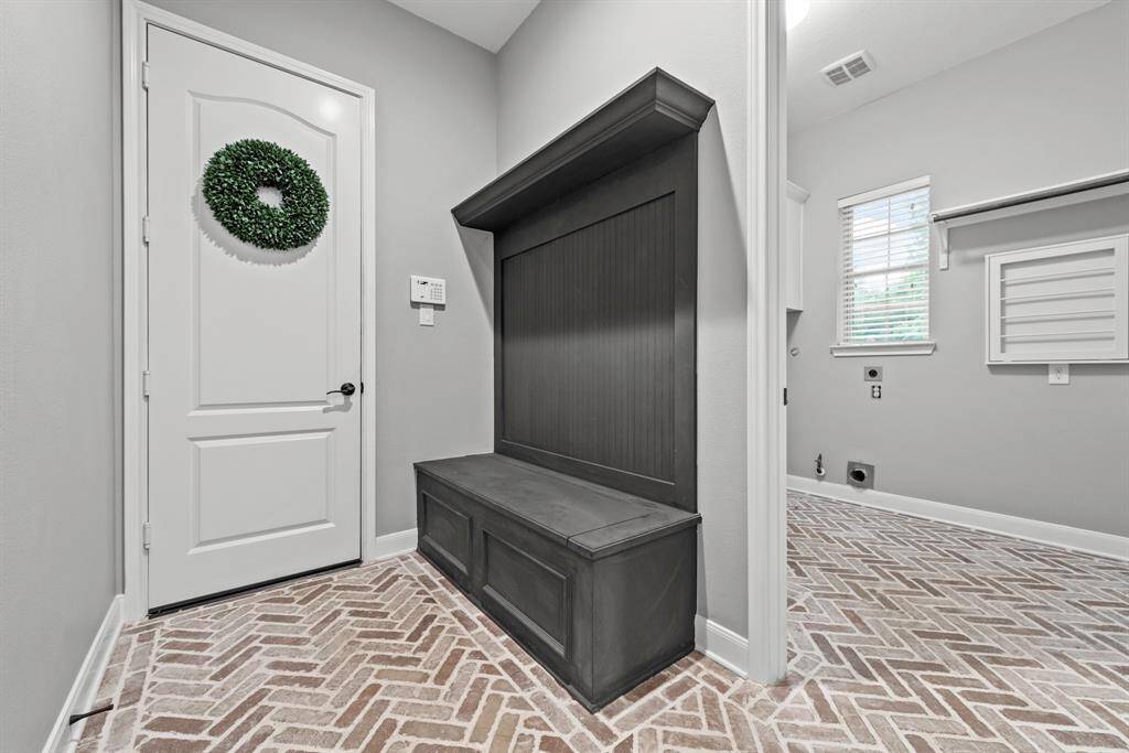 Entrance to 3 of the 4 car garage area, brick floor at mud and laundry room greeted by a wood stained drop zone station.