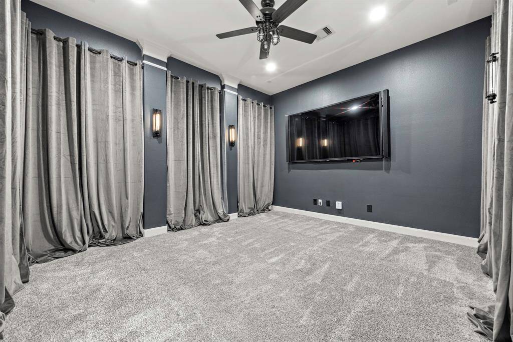 Downstairs media room lined with lush velvet curtains and linear wall scones ready to showcase your favorite flicks.