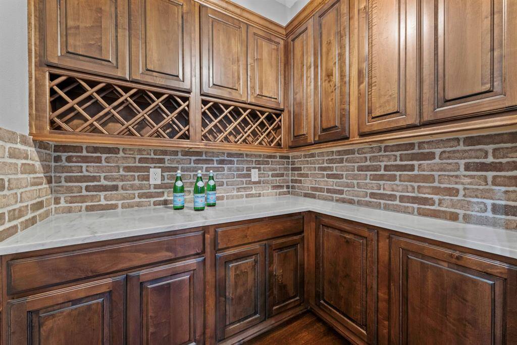 Wine room with stained upper and lower cabinets, wine rack and brick backsplash.