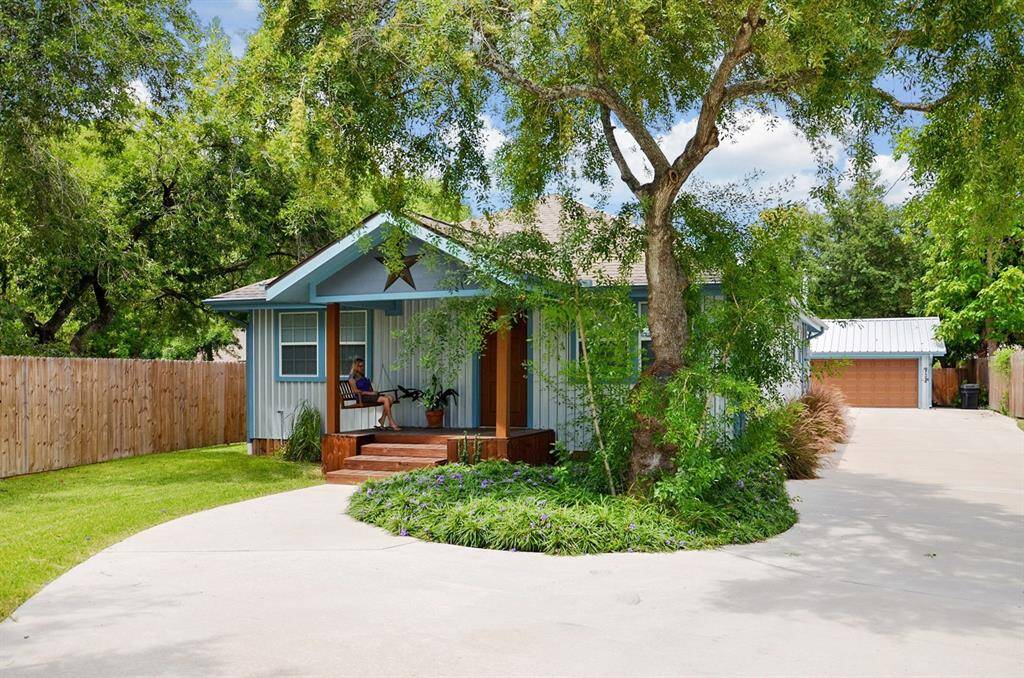 Charming single-story home with a cozy front porch, nestled among mature trees. It features a well-maintained lawn and a spacious driveway leading to a detached garage. Perfect for enjoying outdoor living.