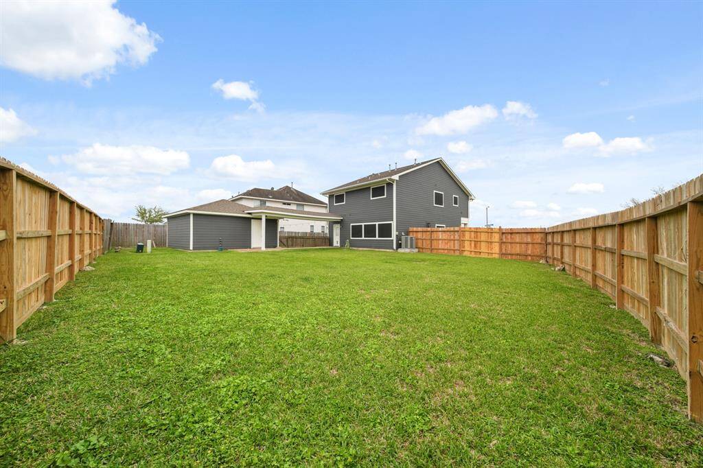 Spacious fenced backyard with a large grassy area, ideal for outdoor activities. The modern two-story home has a dark exterior and a covered patio, offering ample space and privacy.