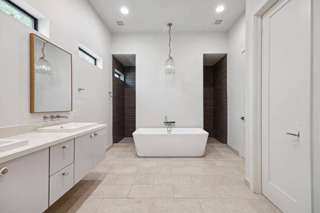 The primary bathroom features tile floors, dual sinks, huge dual sided walk-in shower, and soaking tub with a designer chandelier above!