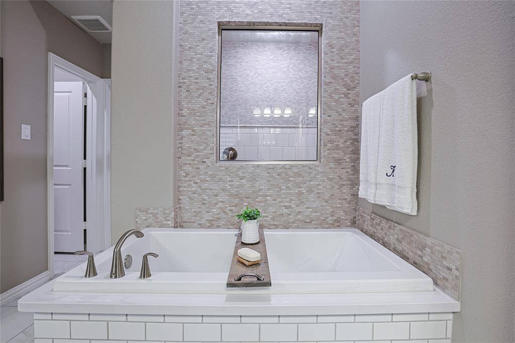Fully tiled accent wall behind the soaking tub, which is surrounded by Silestone.