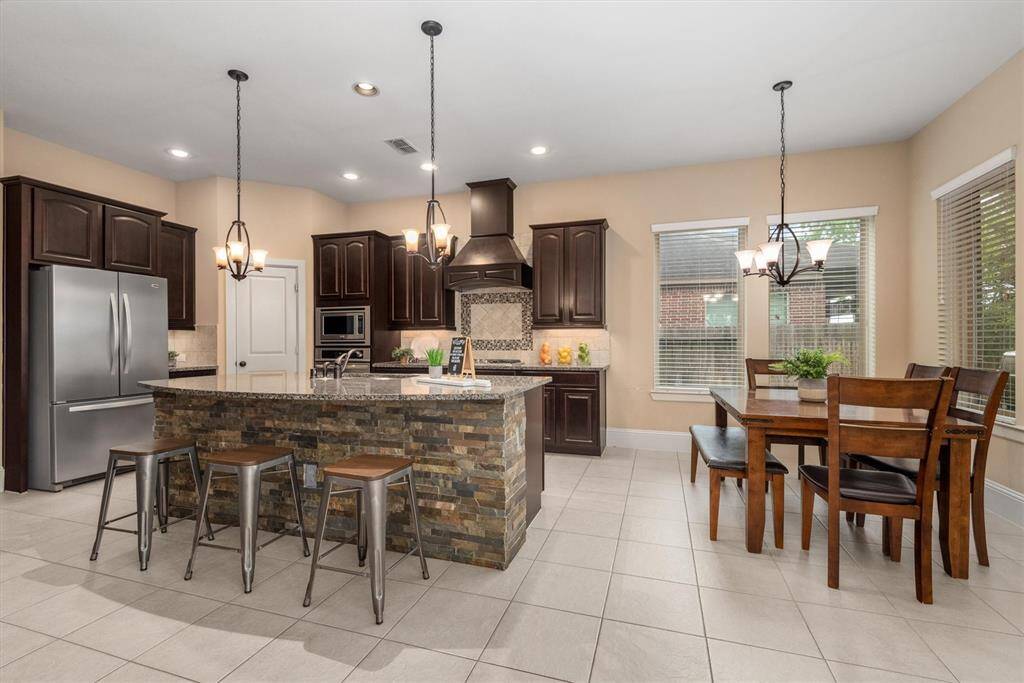 The stunning kitchen blends functionality and style with the sleek rich wood cabinets, granite countertops, and the stacked tile on the island.