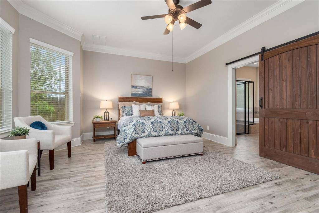 The spacious primary bedroom features stylish plank flooring, crown molding and a bay window.  The stylish barn door leads to the en-suite bathroom.