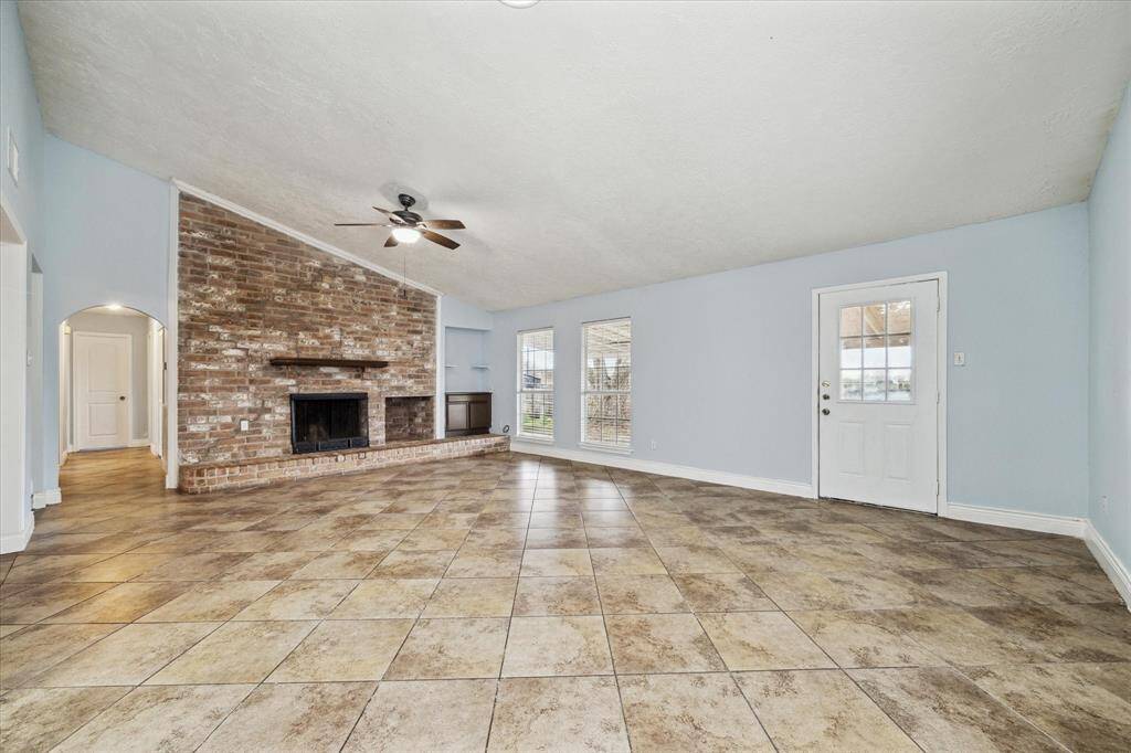 The living room features a high ceiling, a brick fireplace, and large windows that let in plenty of natural light.