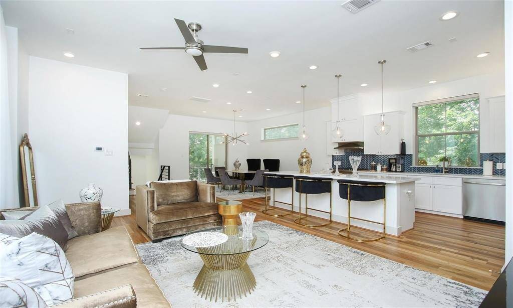 Modern kitchen featuring whitecabinetry, stainless steel appliances,herringbone tile backsplash, and a largewindow overlooking greenery.