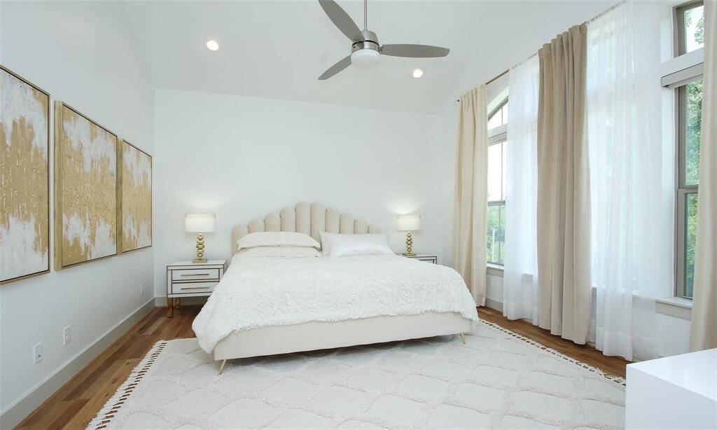 The bright, spacious primary bedroom on the 3rd floor features hardwood floors, modern decor, and ample natural light from tall windows with elegant draperies.