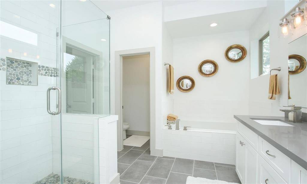 Another view of this beautiful ensuite bathroom with a double-sink, soaking tub, separate shower, and sconce lighting.