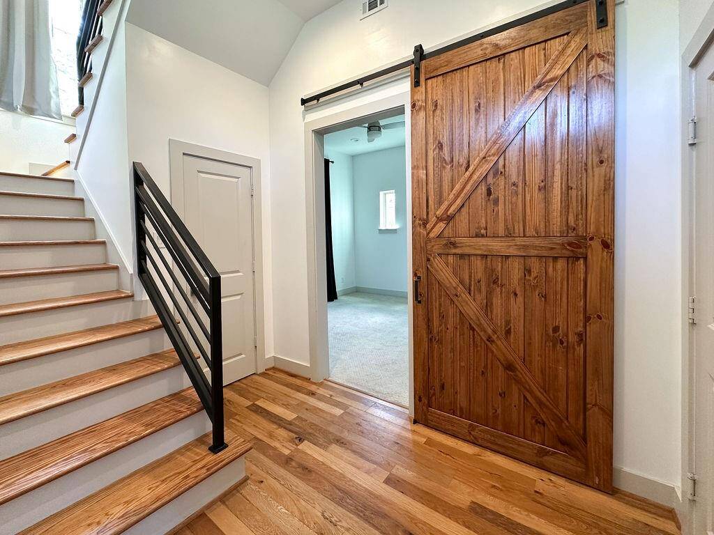 Warm & inviting interior with a stairway to the left featuring wooden steps and a sleek metal railing. A gorgeous barn-style wooden door leads to the first of two secondary bedrooms.