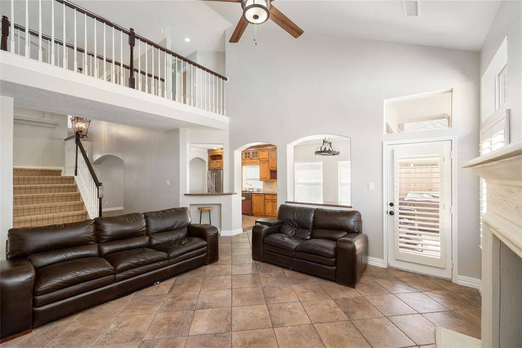 This expansive living room offers soaring ceilings, timeless tile flooring, and an elegant staircase that adds architectural interest. A loft-style second level enhances the open feel, while a patio door with plantation shutters invites in natural light and outdoor views. Seamlessly connected to the kitchen, the layout is designed for both everyday comfort and effortless entertaining.