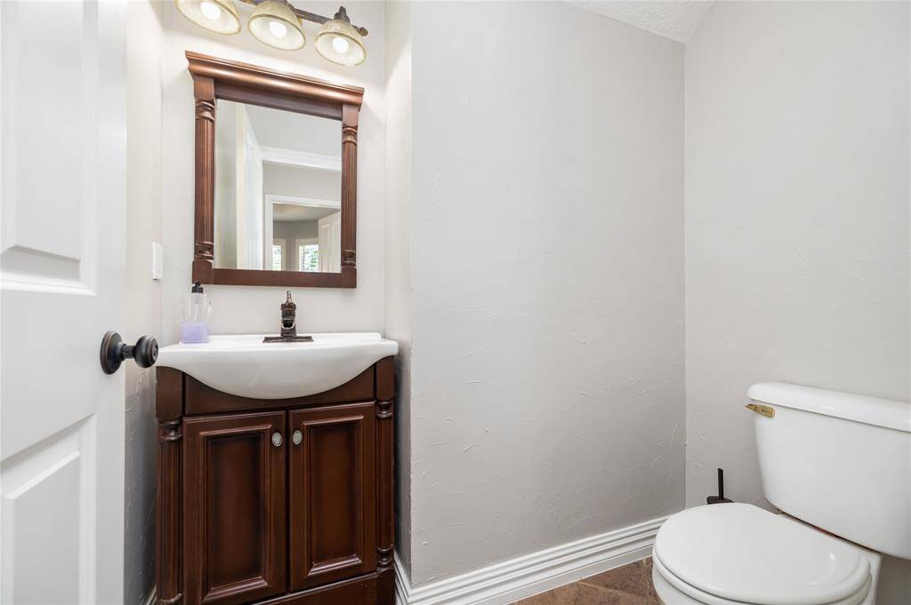 This well-appointed half bath offers everyday convenience with a classic wooden vanity, a white sink, and a timeless light fixture. Neutral walls and a clean design make it a practical and welcoming space for guests.