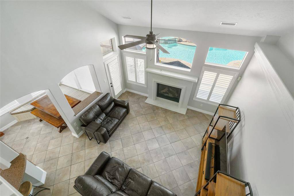 Take in the impressive scale of the living room below—where soaring ceilings, expansive windows, and a cozy fireplace create a warm and welcoming focal point. The open layout flows seamlessly into the dining area, while views of the sparkling backyard pool enhance the sense of light, space, and serenity.