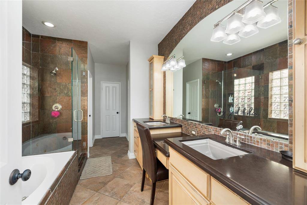 Designed with comfort and elegance in mind, this beautifully appointed bathroom features a spacious double vanity with refined countertops, a large framed mirror, and timeless tile flooring. Enjoy the luxury of a walk-in shower with glass doors and a separate soaking tub—perfect for unwinding after a day spent at the nearby country club or relaxing in your private backyard retreat.