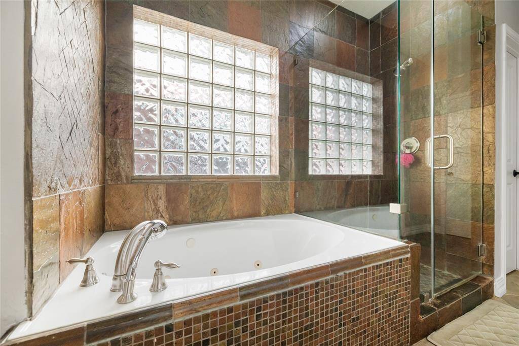 Indulge in everyday luxury with this serene bathroom retreat, where a corner whirlpool tub with polished chrome fixtures invites you to unwind in style. Elegant slate tile surrounds the tub and continues into the glass-enclosed shower, while glass block windows bathe the space in soft, natural light—creating a spa-like ambiance with timeless charm.
