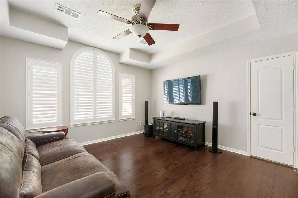Warm hardwood floors, generous windows with classic shutters, and a ceiling fan create a bright and comfortable atmosphere in this flexible upstairs space. Whether used as a media room, game room, or second living area, its open layout and natural light make it a perfect place to relax, entertain, or unwind with family.