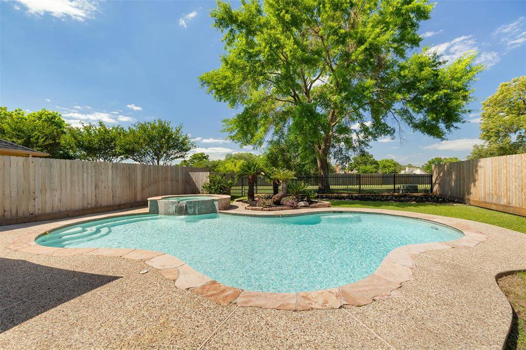 This serene backyard offers the perfect escape, featuring a beautifully designed swimming pool surrounded by a stone walkway. Lush greenery and a mature tree provide both privacy and a peaceful atmosphere, creating an ideal setting for relaxation and outdoor entertainment.