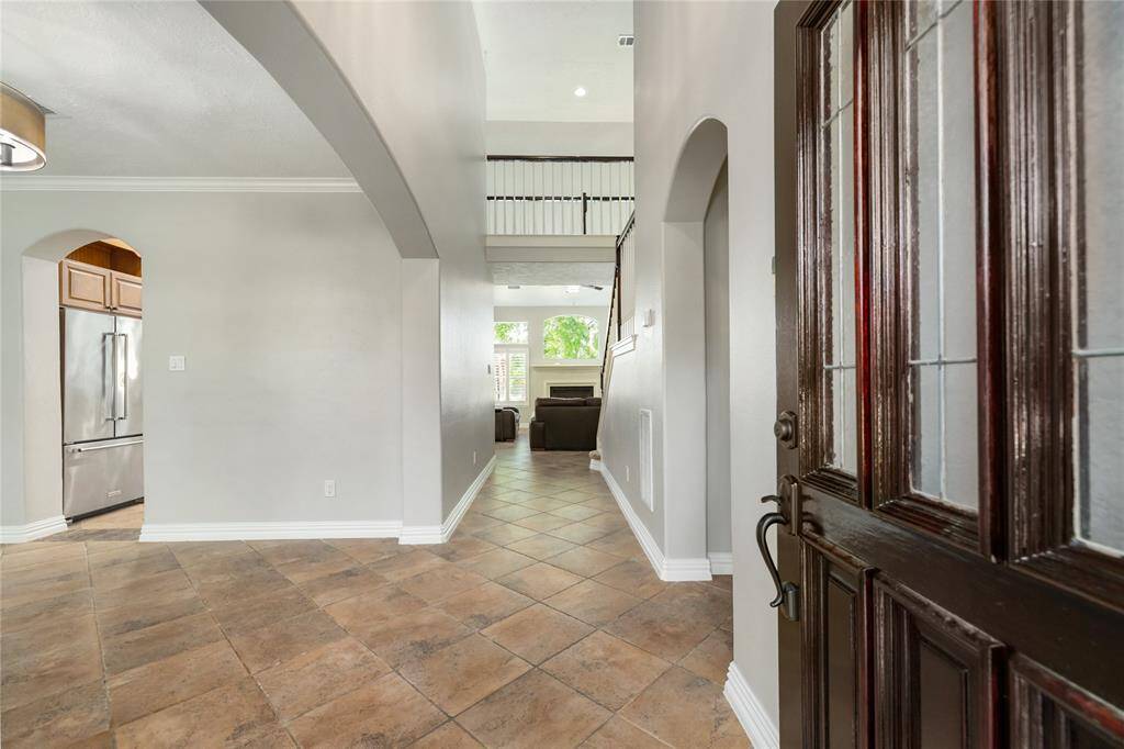 Step through the elegant dark wood door into a bright and inviting entryway, where classic tile flooring and arched openings hint at the timeless design throughout. From this first glance, you're drawn into the heart of the home—an open layout filled with natural light and a graceful flow leading to the beautifully updated kitchen beyond.