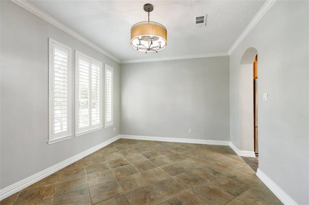This light-filled dining room offers the perfect blend of comfort and sophistication, featuring soft neutral tones, timeless tile flooring, and a graceful arched entryway. Large shuttered windows invite in natural light while maintaining privacy, and a stylish light fixture adds a refined touch—ideal for both intimate dinners and festive gatherings.