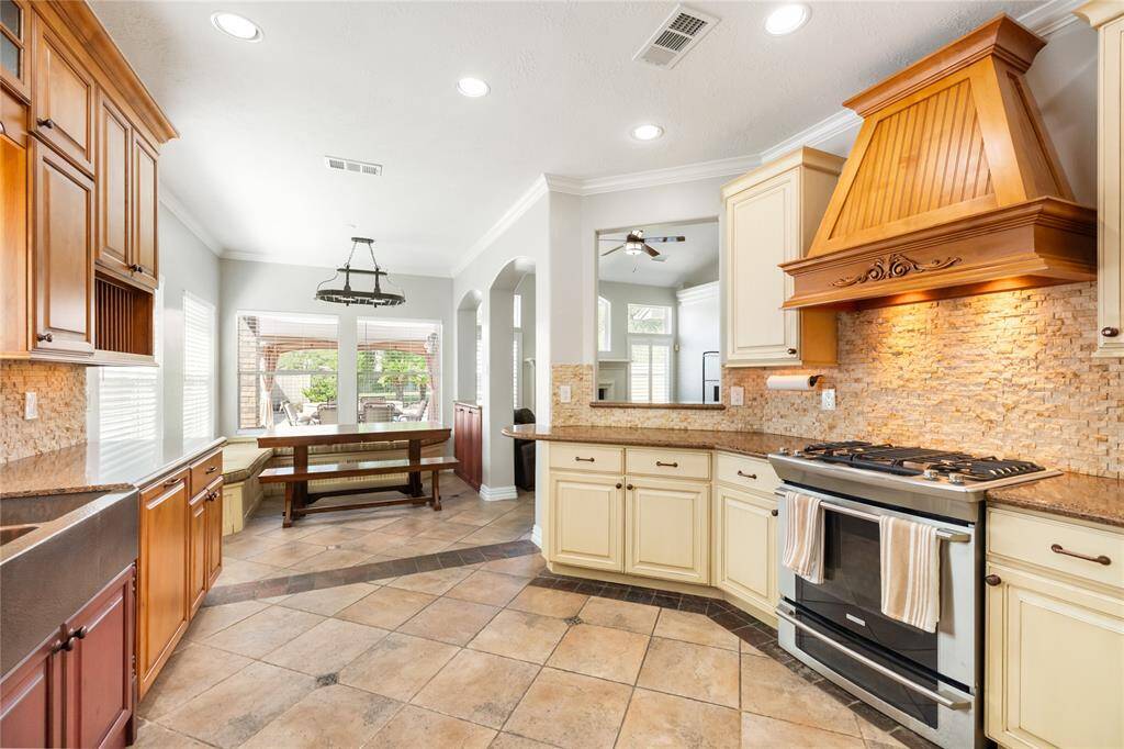The heart of the home, this kitchen combines timeless design with modern luxury, showcasing beautifully updated cabinetry, a striking range hood, and a high-end stove that offers both style and functionality. The detailed tile work adds an elegant touch, perfectly complementing the rich wood finishes and gleaming granite countertops. Recessed lighting enhances the inviting atmosphere, creating the perfect space for both casual meals and gourmet cooking.