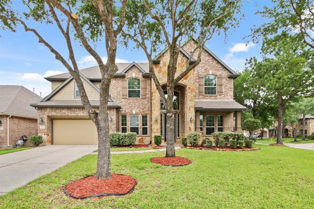 This charming two-story home features a brick and stone exterior, a well-maintained front yard with mature trees, and a spacious driveway leading to a 3 car garage/tandem.