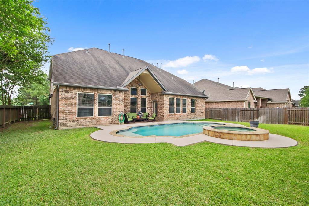 Backyard with a covered patio, a swimming pool, and a spa. The yard is fenced, providing privacy and green space. Ideal for outdoor relaxation and entertainment.