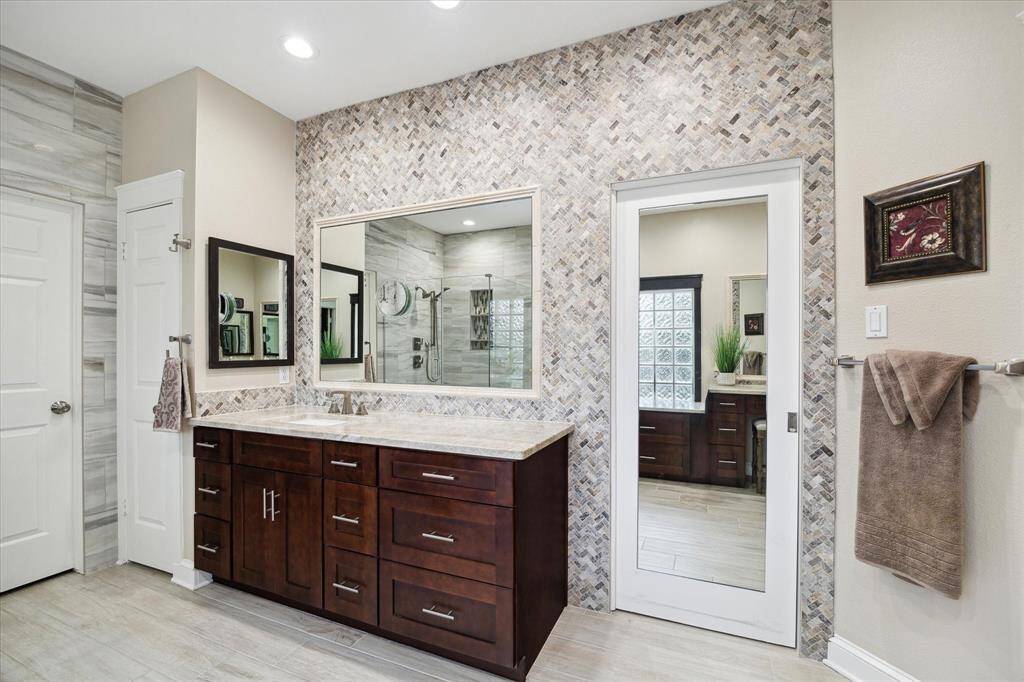 One of two vanities. The wall tile is in a herringbone pattern. The mirrored door is a pocket door that leads to one of two walk in closets.
