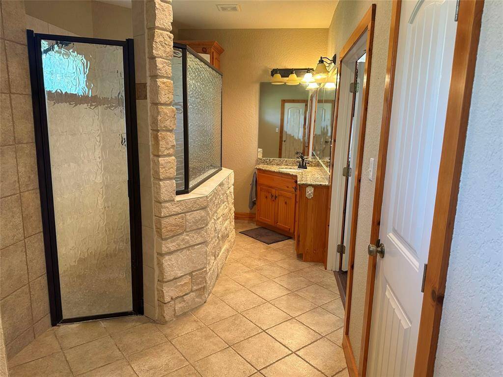 The primary bathroom has a HUGE walk-in custom shower, beautiful wooden shelving, and granite countertops to boast.