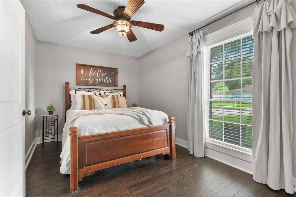 The master suite is a peaceful escape with a lighted ceiling fan, neutral agreeable grey paint, handsome wood floors, an en suite bathroom, and a front yard facing window dressed with 2-inch blinds.