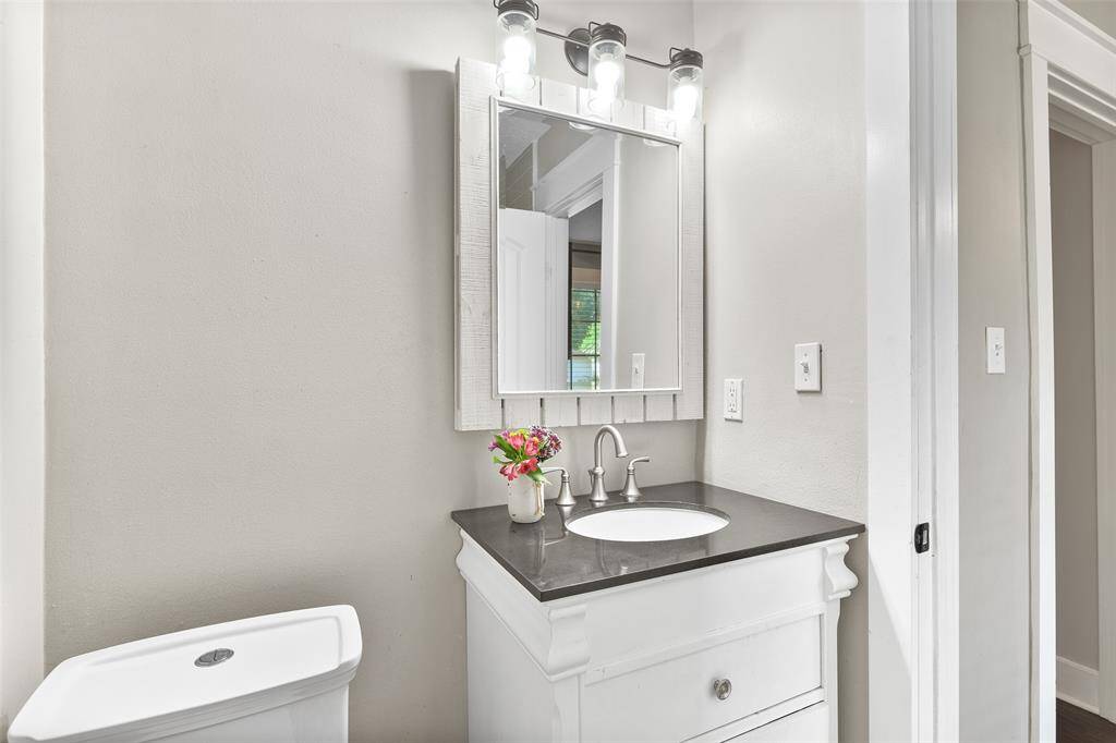 The en suite master bathroom offers a fresh white vanity with a black granite countertop, a single undermount sink, a framed mirror, updated lighting, and a combination bathtub and shower with a beautiful tile surround.