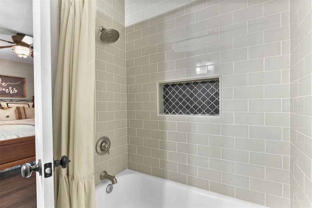 The en suite master bathroom offers a fresh white vanity with a black granite countertop, a single undermount sink, a framed mirror, updated lighting, and a combination bathtub and shower with a beautiful tile surround.