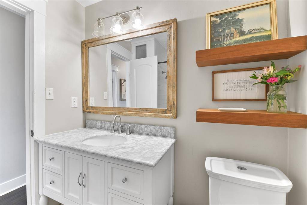 The hall bathroom boasts a white dresser-style vanity with a gorgeous grey and white marble countertop, an undermount basin sink, a framed mirror, designer lighting, and a combination bathtub and shower with a stylishly updated tile surround.