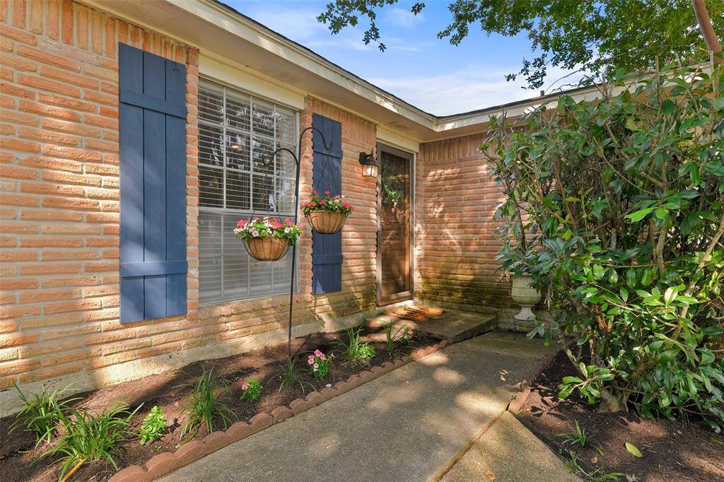 A concrete path leads from the double-wide driveway to the front door of this traditionally styled home with a blush-colored brick elevation, charming painted shutters, a full panel glass storm door, and a stained wood carriage-style front door with a keyless electronic lock.