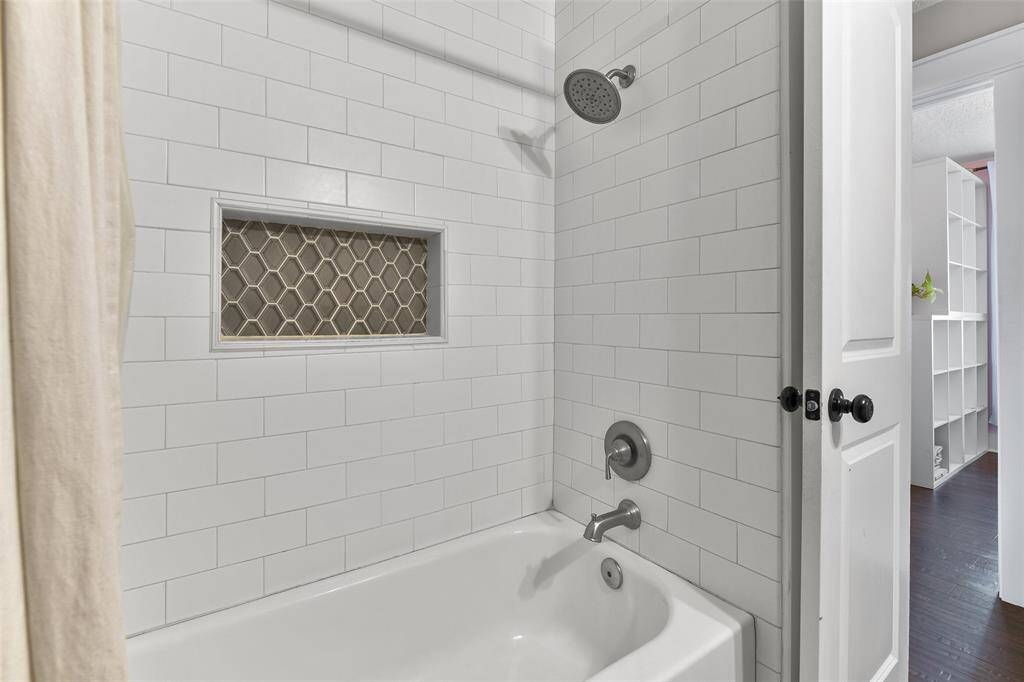 The hall bathroom boasts a white dresser-style vanity with a gorgeous grey and white marble countertop, an undermount basin sink, a framed mirror, designer lighting, and a combination bathtub and shower with a stylishly updated tile surround.