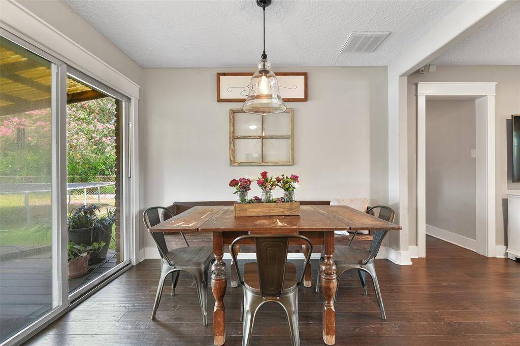 Beyond the family room, you'll find a lovely sunlit dining room with continued engineered wood floors, neutral paint, wide doorways, a beautiful seeded glass bell pendant light, and a sliding glass door to the covered back patio.