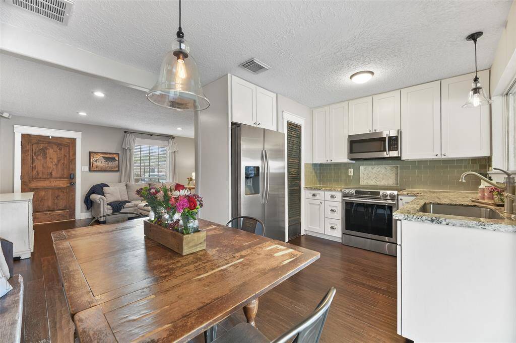 Beyond the family room, you'll find a lovely sunlit dining room with continued engineered wood floors, neutral paint, wide doorways, a beautiful seeded glass bell pendant light, and a sliding glass door to the covered back patio.