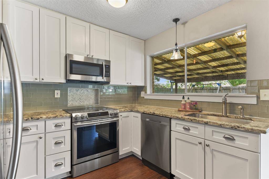 The kitchen has been masterfully updated to include fresh white cabinetry with modern hardware, gleaming granite countertops, and a glass tile backsplash with a herringbone accented inset that's perfect for spices while cooking.